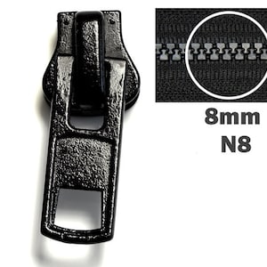 Könnte beinhalten: Schwarzer Metall-Reißverschluss-Schieber mit rechteckiger Form und einer kleinen Öffnung. Der Reißverschluss-Schieber ist für einen 8 mm Reißverschluss, auch bekannt als N8 Reißverschluss, ausgelegt.