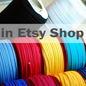 May include: Multiple spools of colorful fabric cord arranged in rows. The collection includes black, white, light blue, red, yellow, turquoise, and dark blue spools. The text "in Etsy Shop" is overlaid across the center of the image.