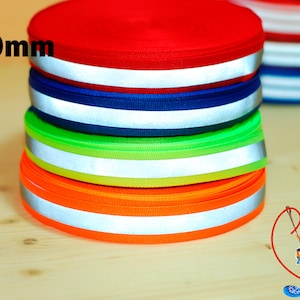 Könnte beinhalten: Eine Rolle reflektierendes Band in den Farben Rot, Dunkelblau, Limettengrün und Orange. Jedes Band hat einen weißen reflektierenden Streifen. Die Breite des Bandes beträgt 20 mm.