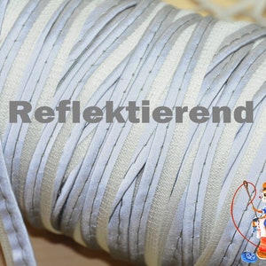 Könnte beinhalten: Nahaufnahme einer Rolle reflektierender silberner und weißer Borte. Die Borte besteht aus einem dünnen, flexiblen Material und hat eine reflektierende Oberfläche. Der Text "Reflektierend" ist auf der Rolle sichtbar.