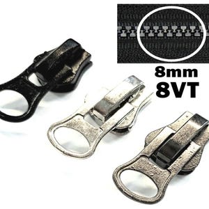 Könnte beinhalten: Drei Reißverschluss-Schieber in verschiedenen Ausführungen. Einer ist schwarz, einer ist silber und einer ist eine Kombination aus Silber und Schwarz. Die Reißverschluss-Schieber sind 8 mm und 8VT.
