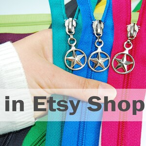 May include: A collection of colorful fabric zippers featuring silver-toned metal pulls with a star-shaped design enclosed in a circular frame. The zippers are displayed in various vibrant shades including teal, blue, magenta, green, and dark purple.