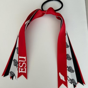 Pode incluir: Um elástico de cabelo de fita vermelha, branca e preta com o texto "ESU" e um logotipo branco com asas.