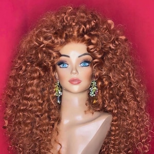 Könnte beinhalten: Ein Schaufensterpuppenkopf mit einer voluminösen, lockigen, kupferfarbenen Perücke. Die Schaufensterpuppe hat blaue Augen und trägt bunte, baumelnde Ohrringe. Der Hintergrund ist ein kräftiges Rot, das einen starken Kontrast zur Perücke und der Schaufensterpuppe bildet.