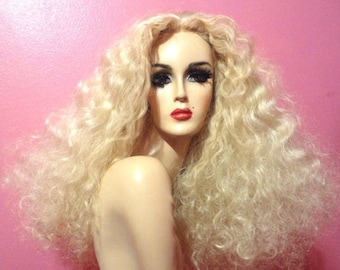 May include: A long, blonde wig with loose curls. The wig is styled in a voluminous, cascading style.