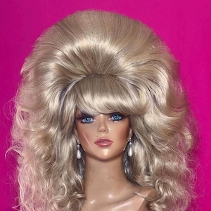 Könnte beinhalten: Blonde Perücke mit großem Toupier und Kaskadenlocken, präsentiert auf einem Schaufensterpuppenkopf mit blauen Augen und Perlenohrringen. Die Perücke hat einen Vintage-Stil, geeignet für Kostüme oder Bühnenproduktionen.