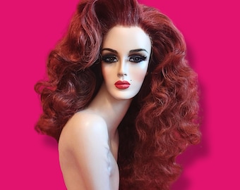 May include: A mannequin head featuring long, voluminous, wavy auburn hair styled with a high side-swept part. The mannequin has a pale complexion, defined dark eyebrows, heavy black eyeliner, long eyelashes, and bright red lipstick.