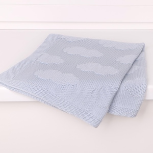 May include: A light blue knitted baby blanket featuring a repeating pattern of soft, textured clouds. The blanket has a distinct border with a fine knit stitch, while the central area displays the cloud motifs in a slightly raised, knit texture.
