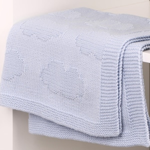 May include: A light blue knitted blanket featuring a repeating pattern of textured clouds. The blanket has a wide, ribbed border along the edges and a soft, consistent knit construction throughout the entire piece, showcasing a uniform color.