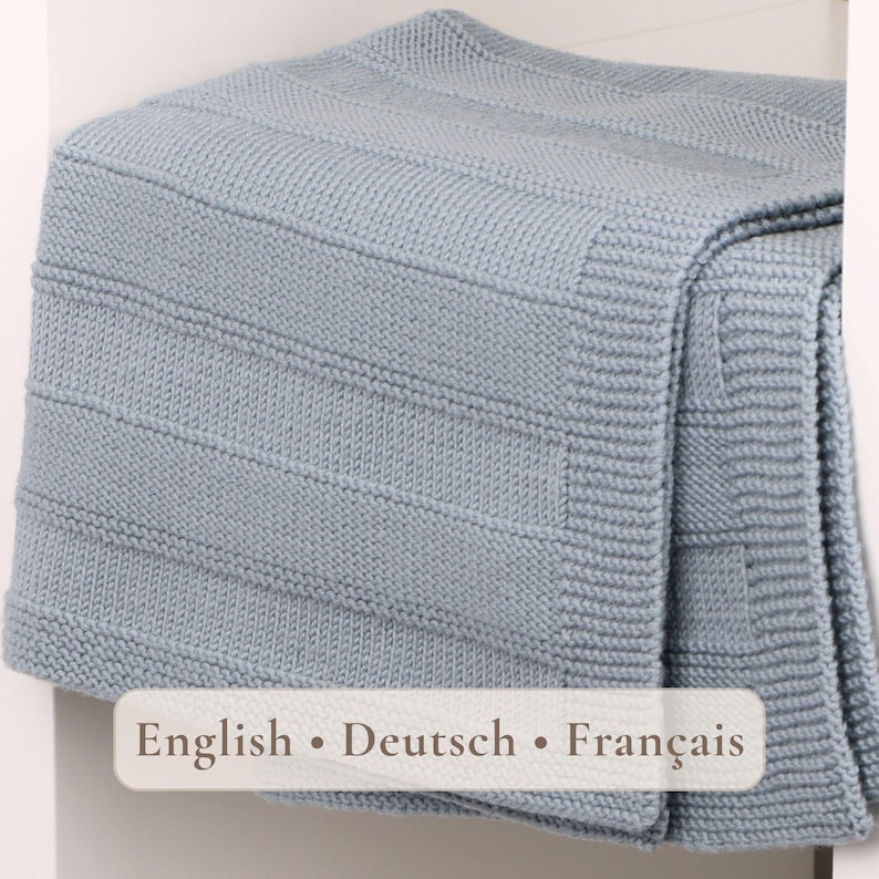May include: A light blue knitted blanket featuring a textured pattern of alternating horizontal stripes and garter stitch borders. The fabric has a consistent, uniform weave throughout, and the text "English &bull; Deutsch &bull; Fran&ccedil;ais" is printed on a label.