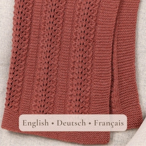 May include: A terracotta-colored knitted scarf featuring vertical columns of intricate lace stitch patterns alternating with sections of garter stitch. The fabric has a textured appearance with a consistent rust-toned yarn throughout the entire piece.