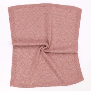 May include: A dusty rose knitted blanket featuring a repeating heart pattern throughout the center panel. The blanket is finished with a wide, textured garter stitch border along all four edges, creating a soft and uniform appearance.