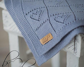 Könnte beinhalten: Eine hellblaue gestrickte Babydecke mit Herzmuster und einem braunen Etikett mit der Aufschrift "Beloved".