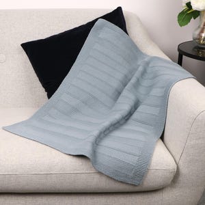 May include: A light blue knitted blanket featuring a textured pattern of alternating horizontal stripes and a solid border. The fabric has a consistent weave throughout, showcasing a soft appearance with a defined edge finish and a rectangular shape.