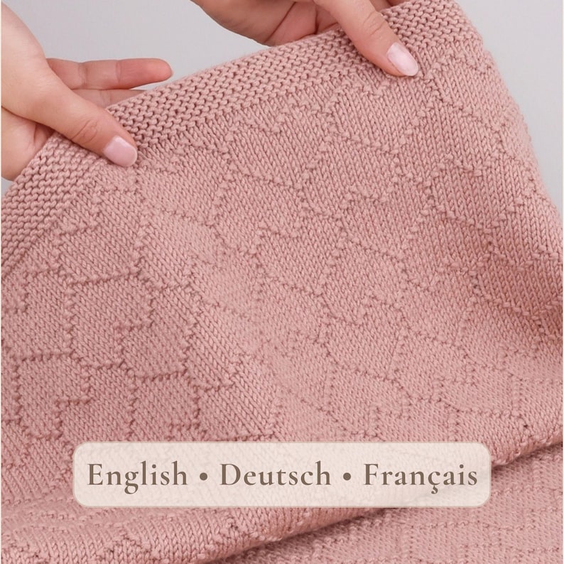 May include: A dusty rose knitted blanket featuring a textured geometric pattern of repeating zig-zag lines and a garter stitch border. The fabric has a consistent knit construction throughout, showcasing a soft, muted pink color palette.