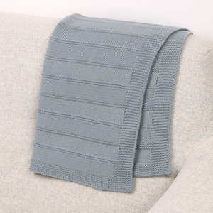 May include: A light blue knitted throw blanket featuring a textured pattern of horizontal rectangular blocks separated by narrow recessed lines, with a wide garter stitch border along the edges, creating a uniform and structured appearance.