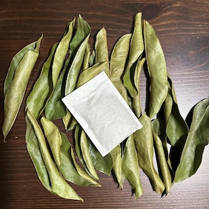Puede incluir: Un montón de hojas verdes secas con una bolsita de té blanca en el centro.