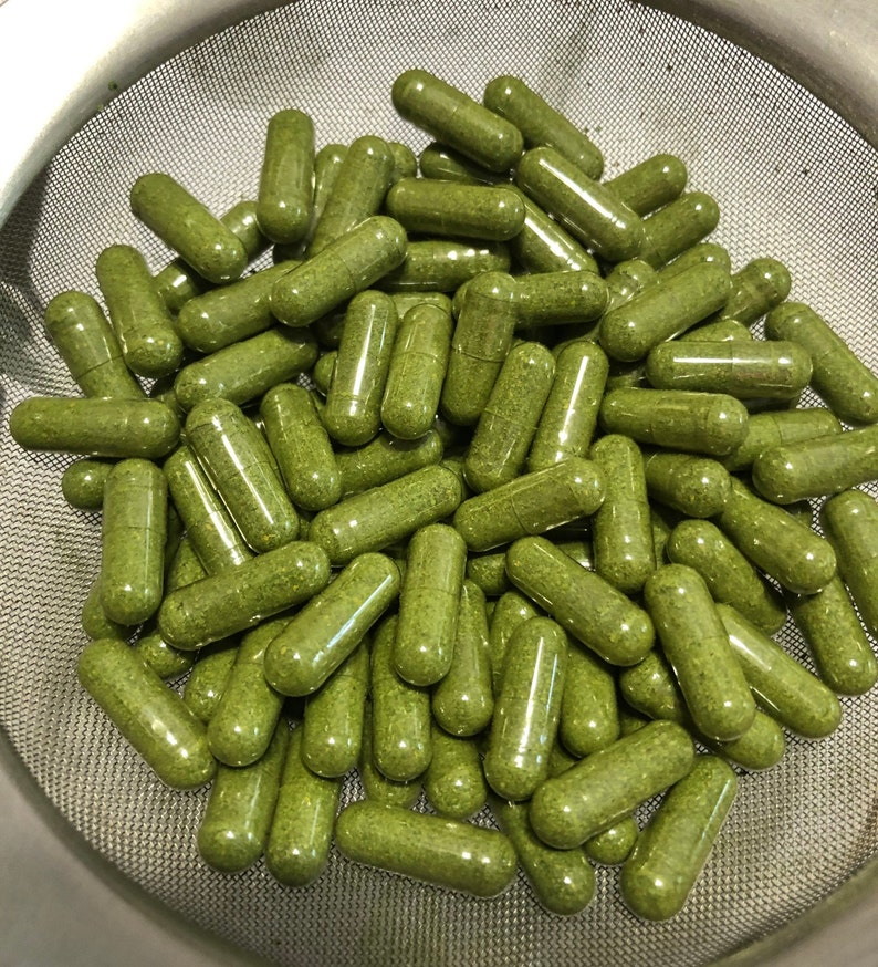 Puede incluir: Primer plano de un colador de metal lleno de c&aacute;psulas verdes. Las c&aacute;psulas est&aacute;n llenas de un polvo verde y est&aacute;n dispuestas en un patr&oacute;n aleatorio.