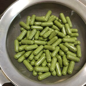 Puede incluir: Un colador de metal lleno de c&aacute;psulas verdes. Las c&aacute;psulas est&aacute;n llenas de un polvo verde.