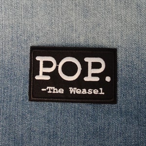 Könnte beinhalten: Schwarz-weiß gestickter Patch mit dem Text "POP. -The Weasel" auf einem Jeans-Hintergrund.