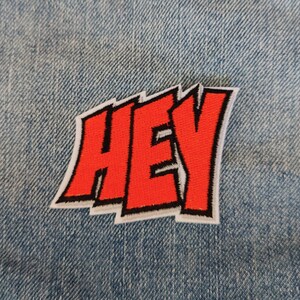 Peut inclure: Patch thermocollant rouge "HEY" sur une veste en jean bleue.