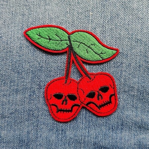 May include: Red cherry with green leaves and two skull faces.