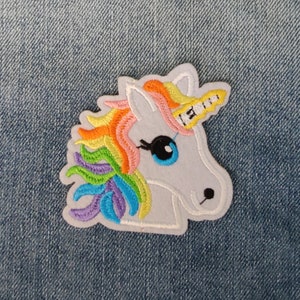 May include: A white unicorn head embroidered patch with a rainbow mane and horn. The patch is on a blue denim background.