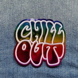 Op de afbeelding: Een strijkbare patch met een regenboogontwerp en witte stiksels met de tekst "Chill Out".