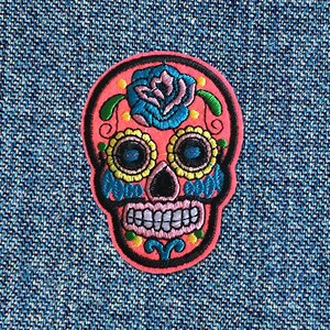 May include: Pink embroidered sugar skull with blue and yellow floral details.