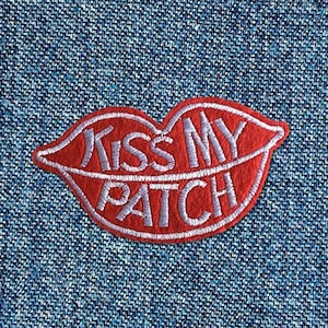 Könnte beinhalten: Roter Filz-Patch mit weißer Stickerei, die "Kiss My Patch" in Form einer Lippenform zeigt.