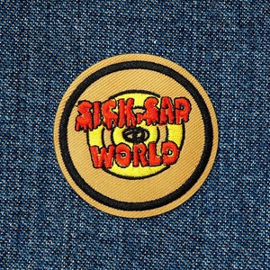May include: A round, brown embroidered patch with a yellow circle in the centre. The text "Sick-Sad World" is written in red dripping letters around the yellow circle.