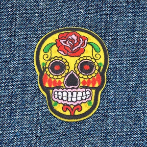 May include: Yellow embroidered skull with a red rose and colourful details. The skull is a traditional Day of the Dead design.
