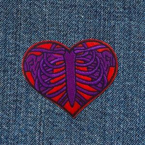 Peut inclure: Patch en forme de cœur rouge avec un motif de cage thoracique brodé en violet.
