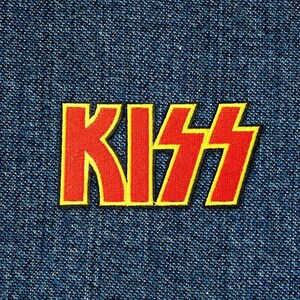 Può includere: Un patch con il logo KISS rosso e giallo su uno sfondo di denim blu.