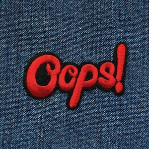 Könnte beinhalten: Roter gestickter Aufnäher mit dem Wort "Oops!" in einer verspielten, cartoonartigen Schrift. Der Aufnäher befindet sich auf einem blauen Jeansstoff.