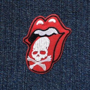 Può includere: Toppa ricamata rossa e bianca di una lingua con un teschio e ossa incrociate all'interno. La lingua sporge e ha un contorno bianco. Il teschio è bianco con occhi neri e un naso nero. Le ossa incrociate sono bianche.