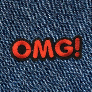 Op de afbeelding: Rode geborduurde patch met de tekst "OMG!" op een blauwe denim achtergrond.