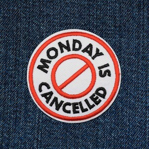 Könnte beinhalten: Ein weißer und roter runder Patch mit dem Text "MONDAY IS CANCELLED" in schwarzen Buchstaben und einem roten Strich durch einen weißen Kreis.