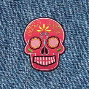 May include: Pink embroidered sugar skull patch with black outlines and yellow and green floral details.