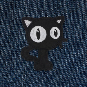 Può includere: Toppa di gatto nero ricamata con occhi bianchi. La toppa è su uno sfondo di denim blu.