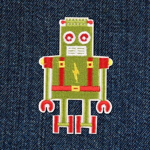 Op de afbeelding: Geborduurde patch met een retro robotontwerp. De robot is voornamelijk olijfgroen met rode en witte accenten. Een gele bliksemschicht staat op de borst van de robot. De patch staat op een blauwe denim achtergrond.