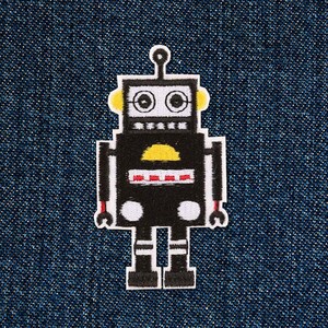 Könnte beinhalten: Schwarzer Roboter-Stickerei-Aufnäher mit gelben und roten Details. Der Roboter hat einen runden Kopf mit zwei großen Augen und eine kleine Antenne oben. Der Roboter hat zwei Arme mit Händen, die wie Schraubenschlüssel aussehen. Der Roboter hat zwei Beine mit schwarzen Stiefeln.