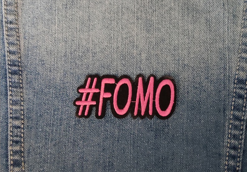 May include: A pink and black embroidered patch with the text "#FOMO" on a denim background.