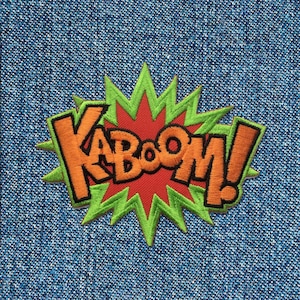 Puede incluir: Un parche bordado verde y naranja con la palabra "KABOOM!" en una fuente de estilo cómic. El parche está sobre un fondo de mezclilla azul.