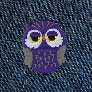 Puede incluir: Parche de búho bordado de color morado con ojos amarillos y cara blanca. El búho está sobre un fondo de mezclilla azul.