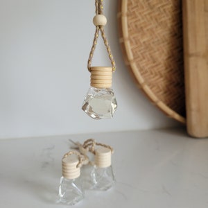 May include: Three glass bottles with wooden caps and a string for hanging. The bottles are clear and have a diamond shape. The bottles are hanging from a string with a wooden bead.