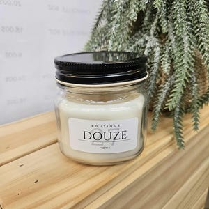 Peut inclure: Une bougie blanche dans un pot en verre transparent avec un couvercle noir. Le pot est doté d'une étiquette blanche sur laquelle est imprimé le texte "Boutique Douze Home".