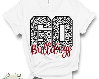 May include: White t-shirt with the number "61" in a black leopard print design. The word "Bulldogs" is written in a burgundy script font below the number. The shirt is folded and tied at the bottom.