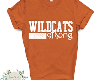 May include: An orange t-shirt with rolled-up sleeves. The shirt features the white text "WILDCATS strong" with a decorative pattern within the word "WILDCATS". The shirt is a Gildan brand.