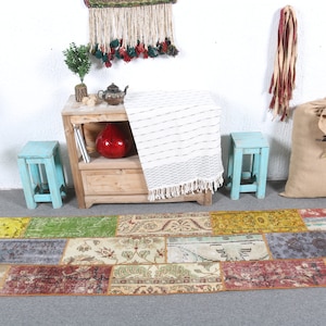 Pode incluir: Um tapete de patchwork colorido com vários tons de vermelho, amarelo, verde e azul. O tapete é feito de diferentes pedaços de tecido costurados juntos. O tapete está colocado sobre um piso cinza em frente a um armário de madeira com uma manta branca.